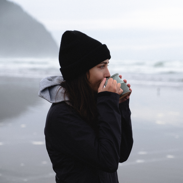 Person in a hooded jacket drinking Peak State Stress Less coffee outdoors
