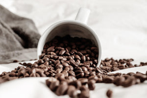 Coffee beans spilling out of a coffee cup onto table.